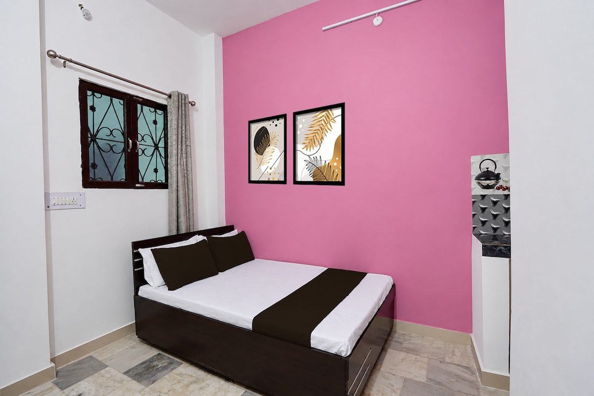 Un dormitorio con cama, ventana con cortinas y dos cuadros en la pared.