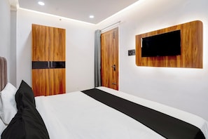 Habitación de hotel con cama, armario de madera, una puerta y televisor montado.