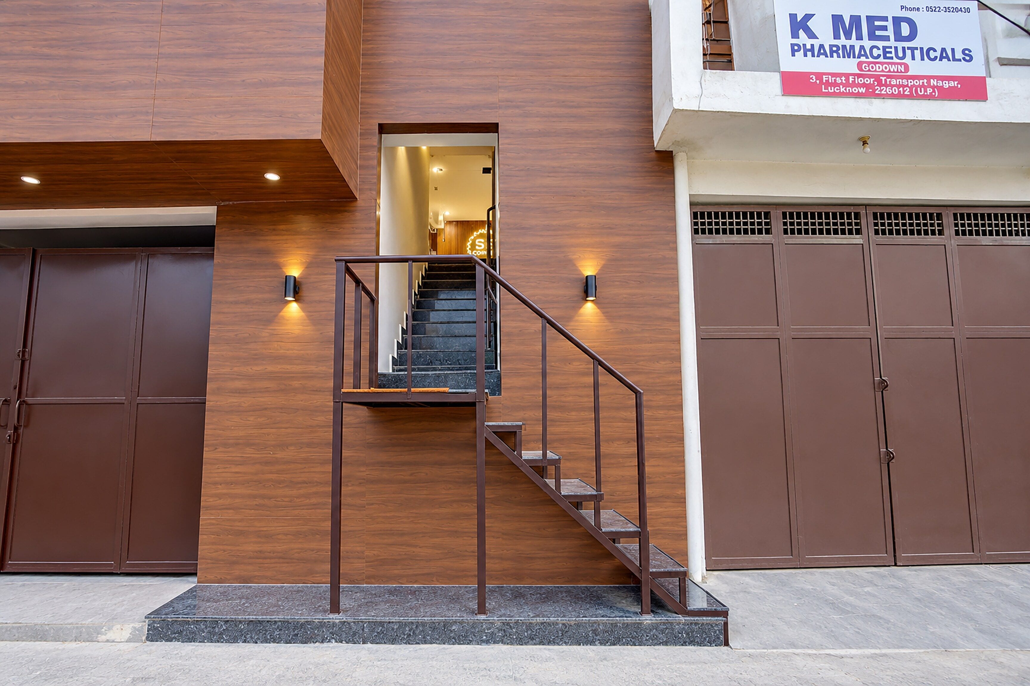 Un edificio moderno con una escalera que conduce a un espacio interior, flanqueado por paneles de madera y un letrero para K Med Pharmaceuticals.