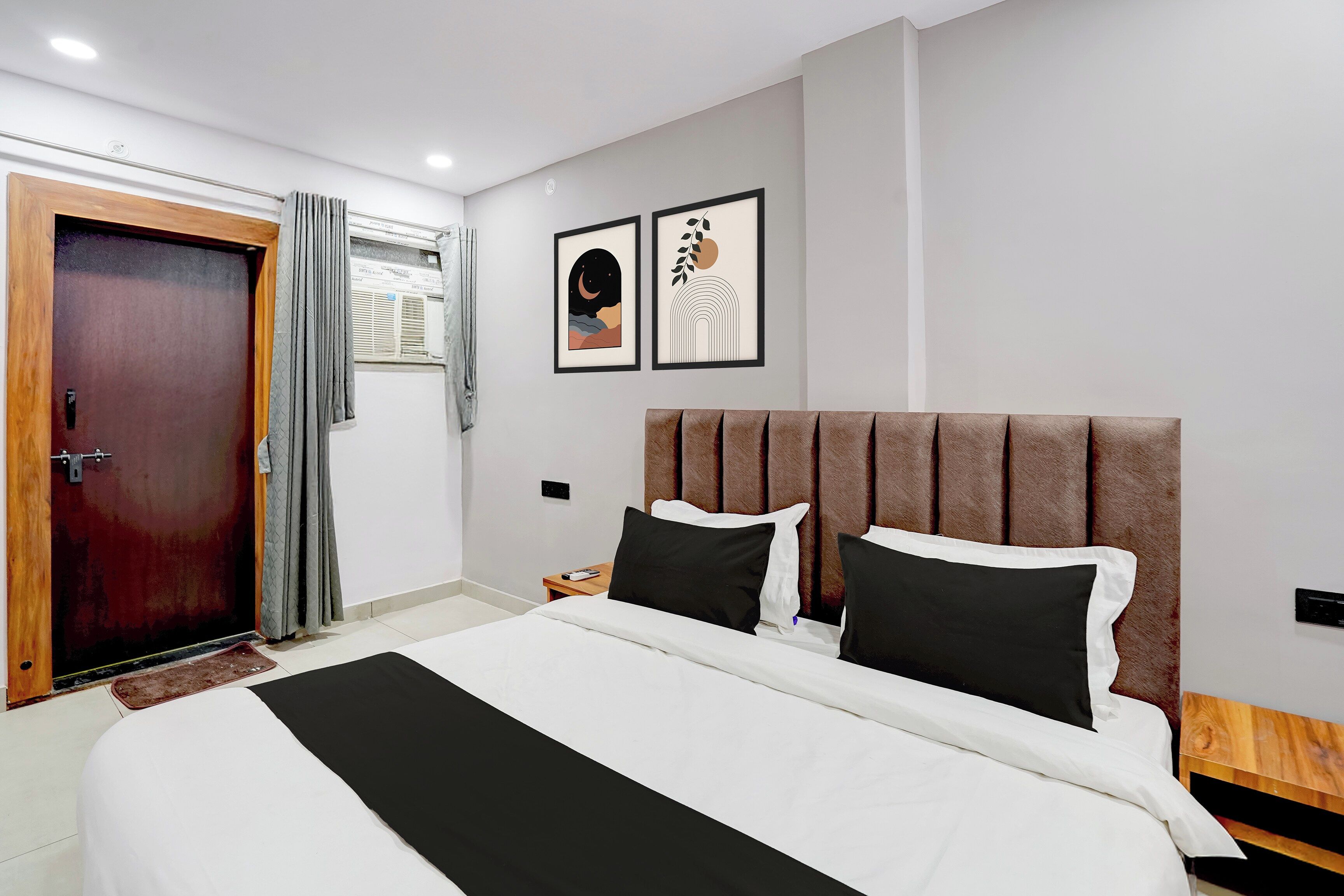 Habitación de hotel con una cama, una puerta de madera, una ventana con cortinas y dos cuadros en la pared.