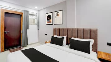 Habitación de hotel con una cama, una puerta de madera, una ventana con cortinas y dos cuadros en la pared.