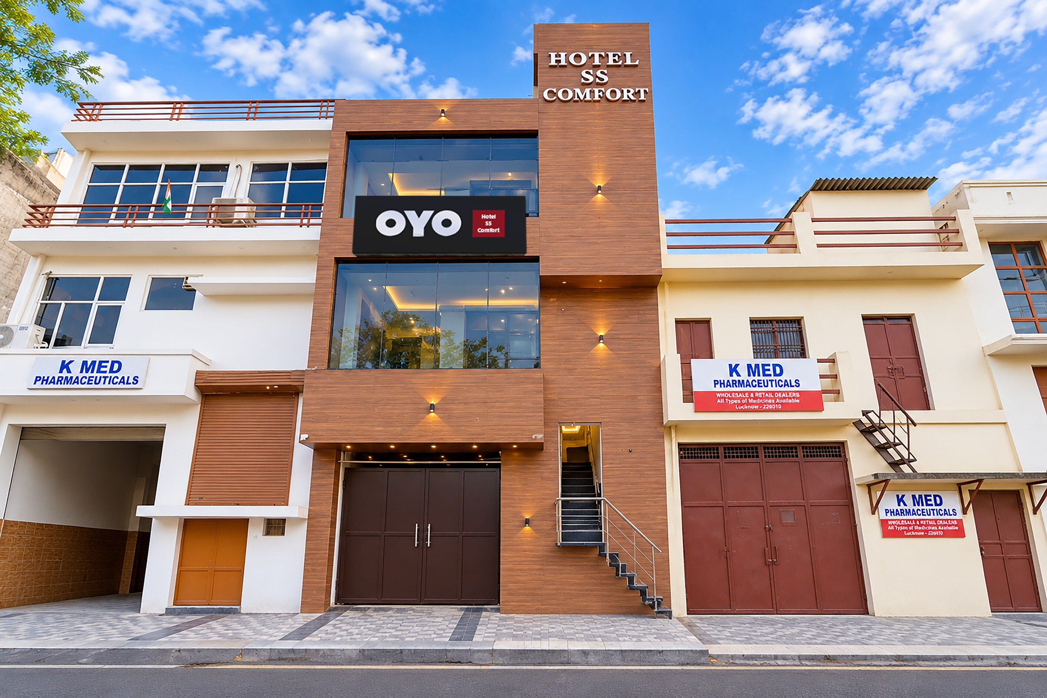 Un hôtel à la façade moderne, avec une enseigne bien visible indiquant « OYO Hotel Comfort », et une enseigne « K MED Pharmaceuticals » au rez-de-chaussée.