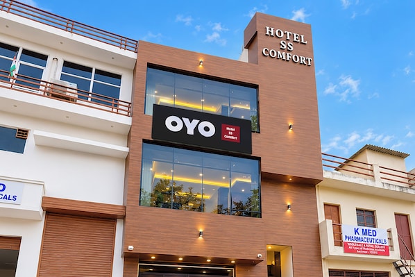 Un edificio de hotel moderno con un cartel destacado que dice 'Hotel SS Comfort' y un cartel más pequeño que dice 'OYO'.
