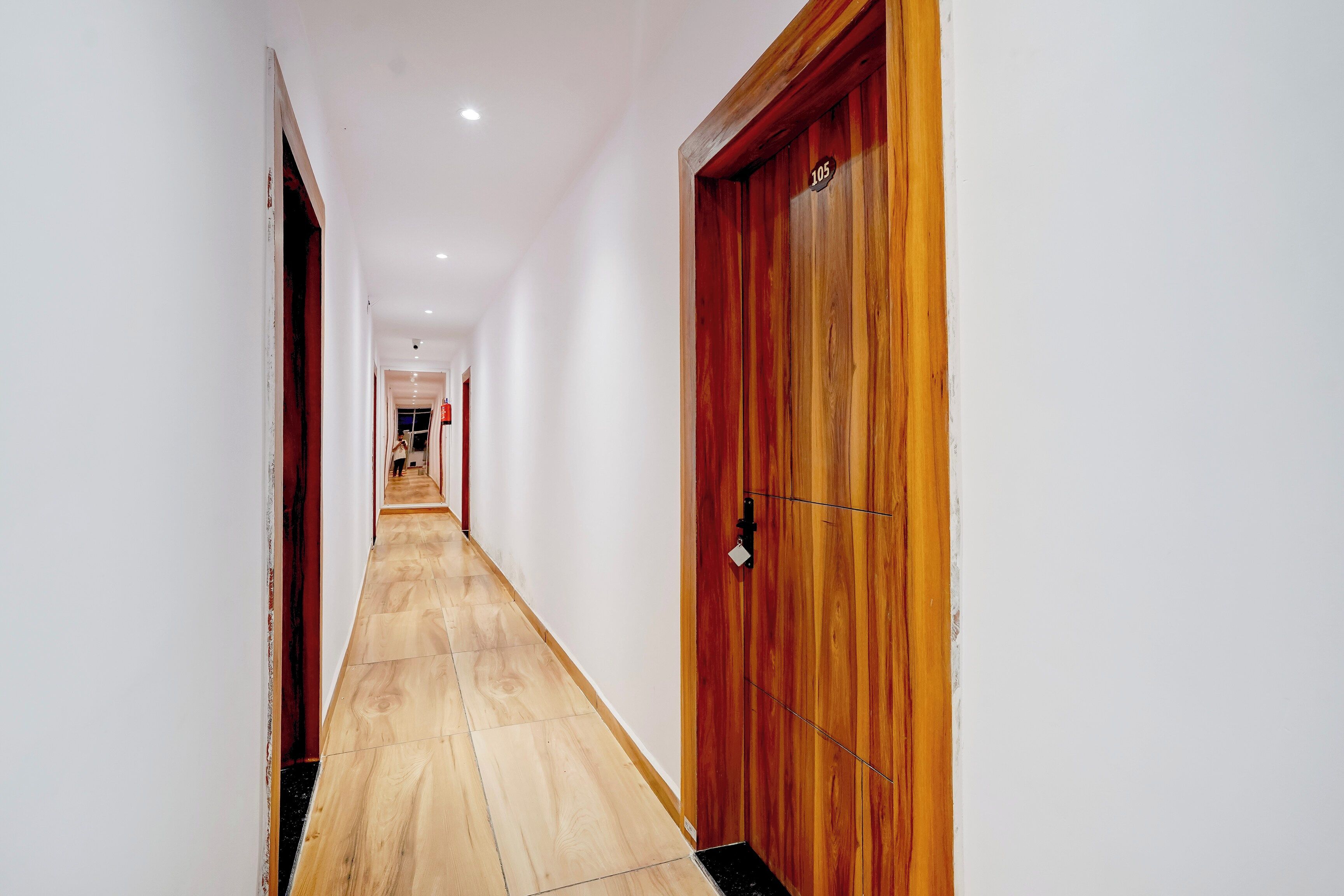 Un couloir avec une porte en bois sur la droite, des murs blancs et un sol carrelé.