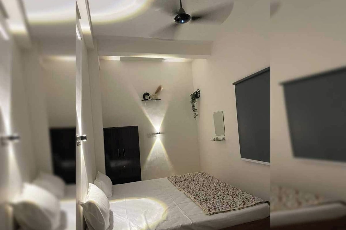 Une chambre à coucher comprenant un lit, une table de chevet, un téléviseur fixé au mur et un ventilateur de plafond.