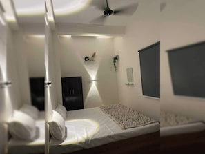 Une chambre à coucher comprenant un lit, une table de chevet, un téléviseur fixé au mur et un ventilateur de plafond.