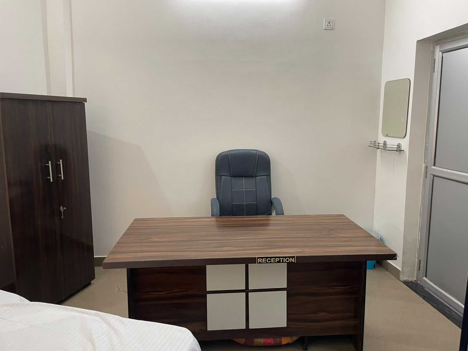 A room with a wooden desk labeled 'RECEPTION,' a blue office chair, a wardrobe, and a door with a mirror.