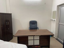 Una habitación con un escritorio de madera con la etiqueta 'RECEPTION', una silla de oficina azul, un armario y una puerta con un espejo.