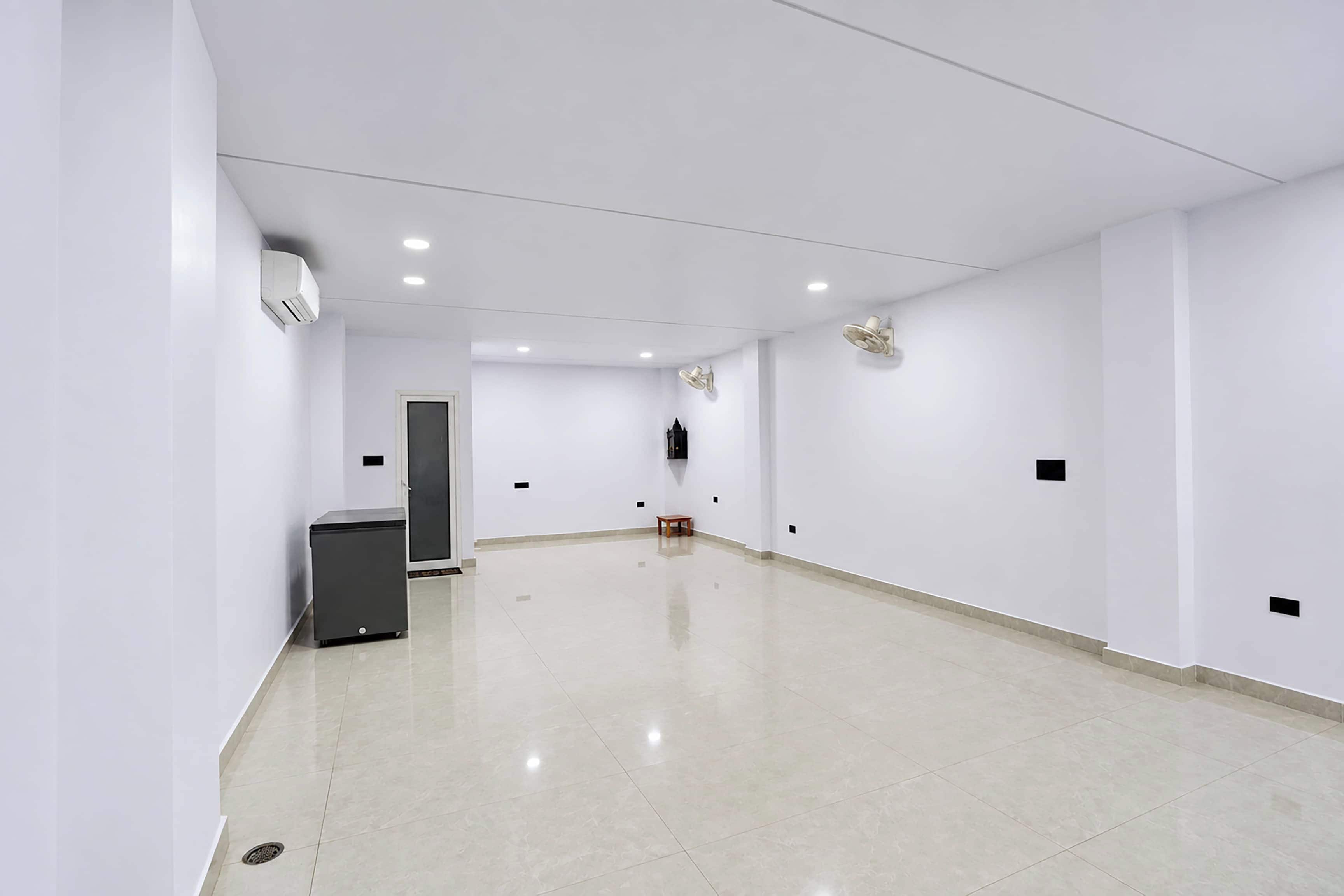 A spacious, well-lit hallway with white walls and a tiled floor, leading to a door at the end.
