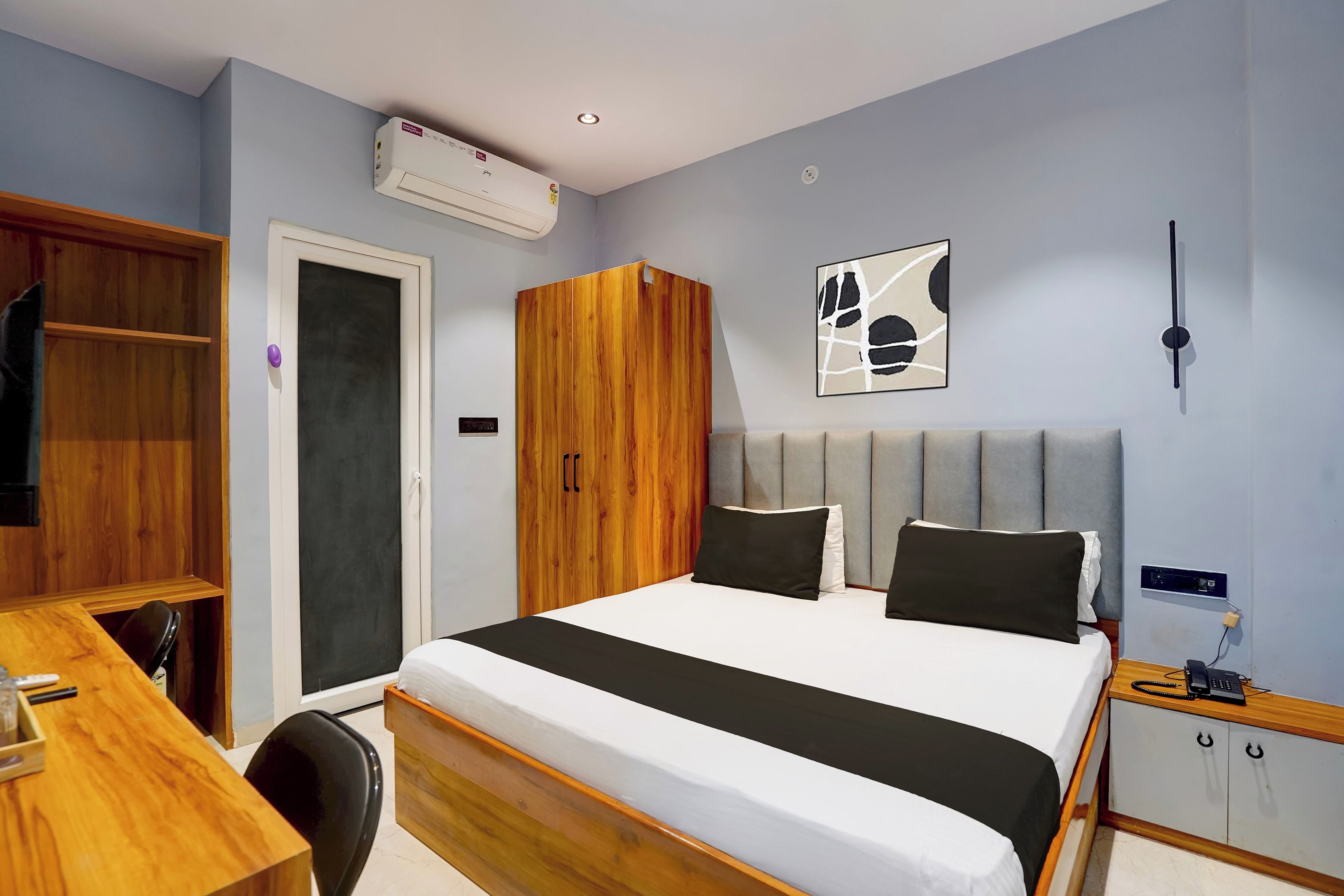 Habitación de hotel con cama, escritorio, armario y aire acondicionado instalado en la pared.