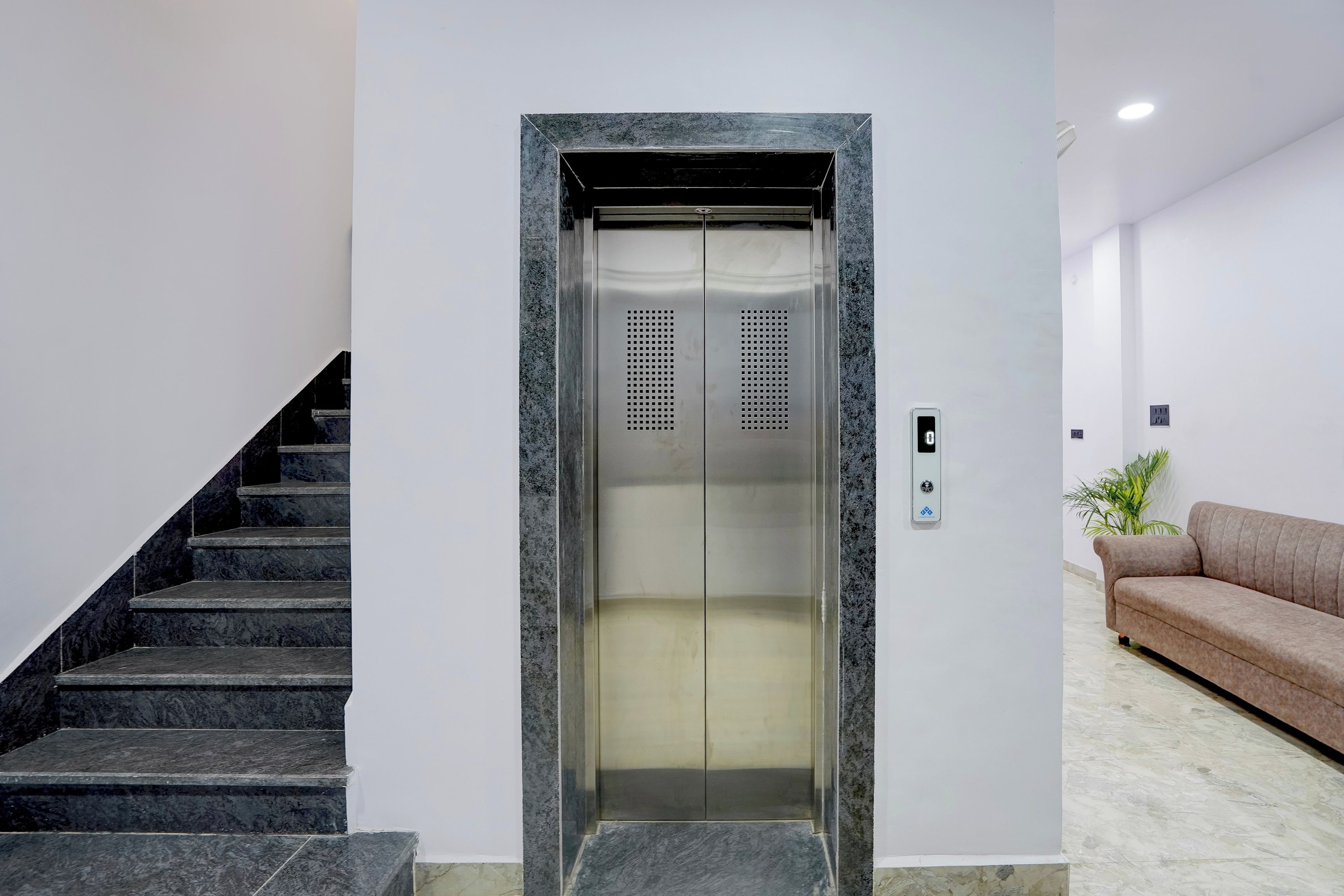 Un ascensor con detalles metálicos, un panel de control con botones y una escalera con escalones de mármol oscuro.