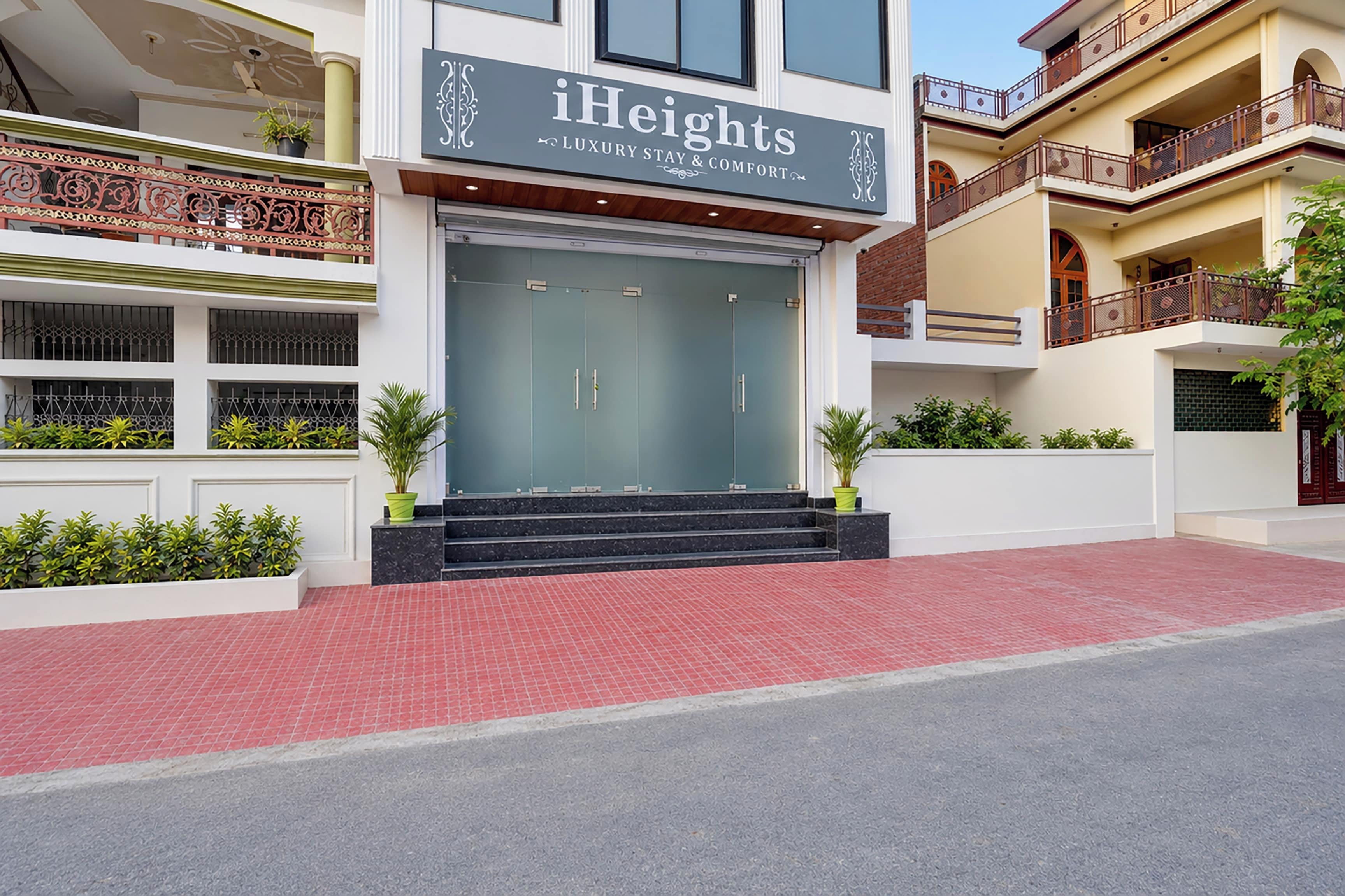 A modern hotel entrance with a glass facade, a sign reading 'iHeights Luxury Stay & Comfort,' and a red-tiled entrance area.
