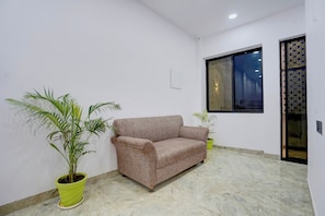 A room with a beige sofa, two potted plants, a window with a geometric pattern, and a marble floor. - Hotel O iHeights Luxury Stay & Comfort (Lucknow)