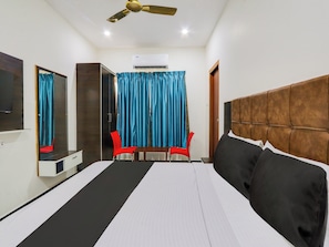 A hotel room with a bed, a ceiling fan, a TV, a mirror, a wardrobe, and two chairs. - Hotel O Arjun Residency (Khammam)