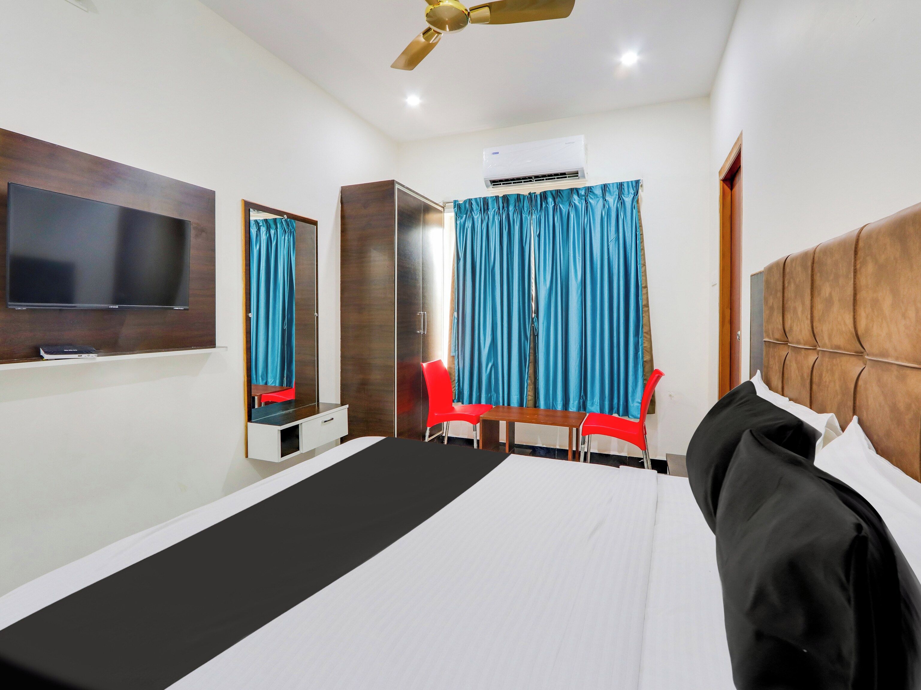 A hotel room with a bed, a TV, a wardrobe, a desk, a chair, and a ceiling fan.