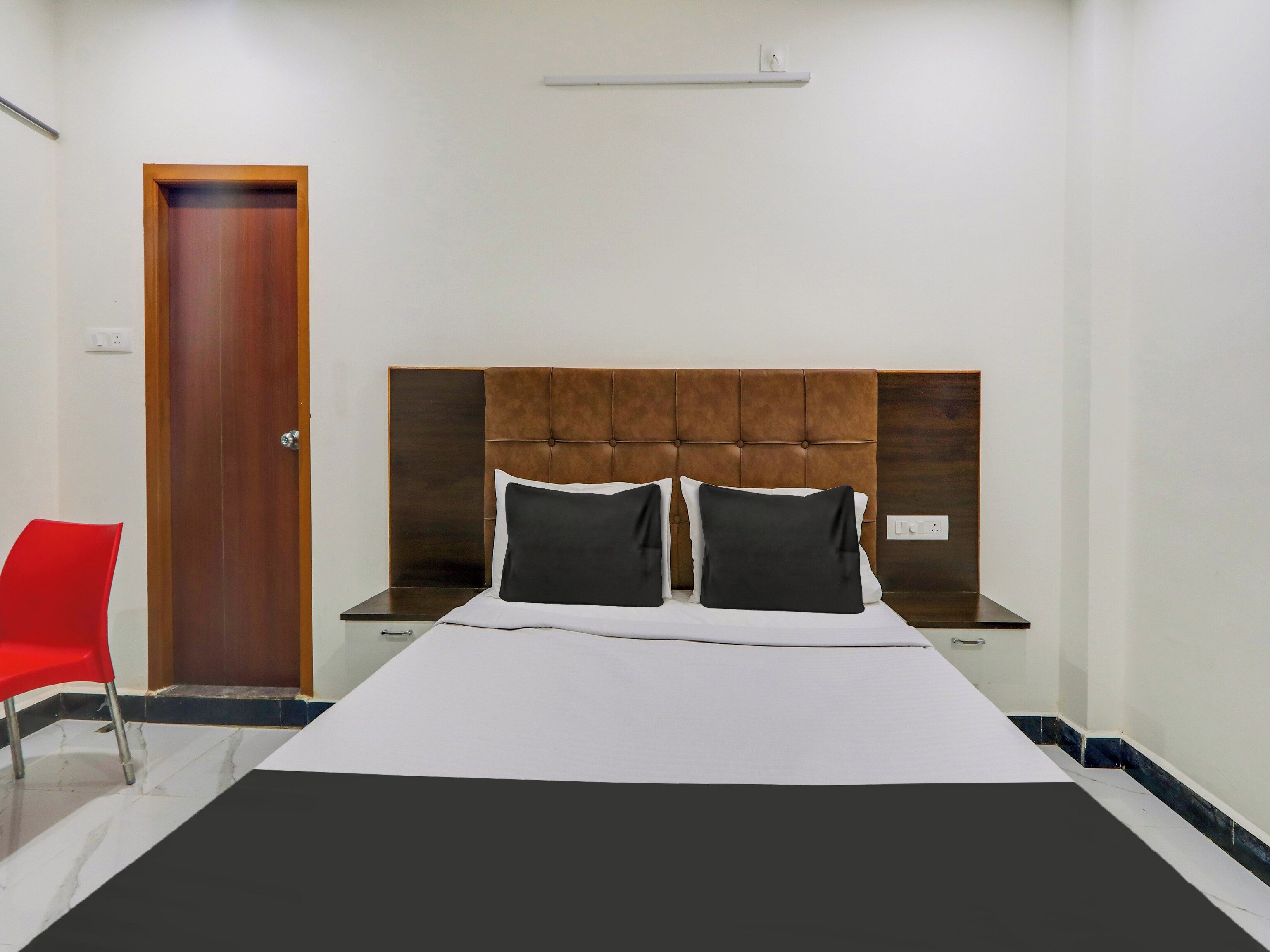 Una habitación de hotel con una cama, una silla roja, una puerta de madera y una mesita de noche.