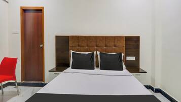 Una habitación de hotel con una cama, una silla roja, una puerta de madera y una mesita de noche.