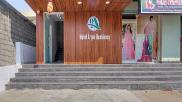La entrada al Hotel Arjun Residency, con fachada de madera, una escalera que conduce a la recepción y un cartel anunciando servicios locales.
