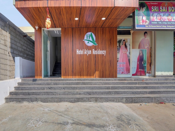 The entrance to Hotel Arjun Residency with a wooden facade, a staircase leading up to the entrance, and a signboard advertising local services.