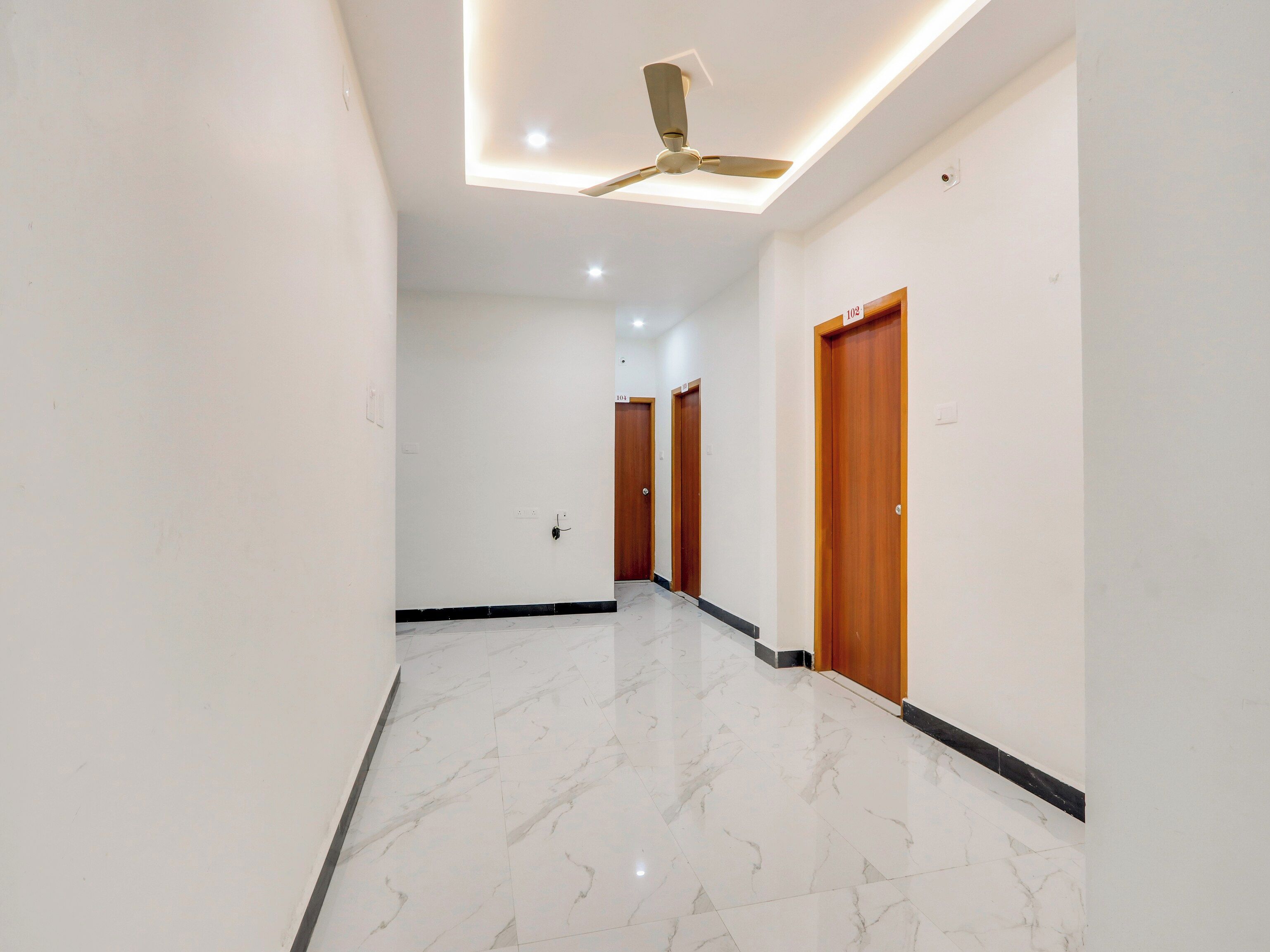 A corridor with marble flooring, wooden doors, and a ceiling fan.