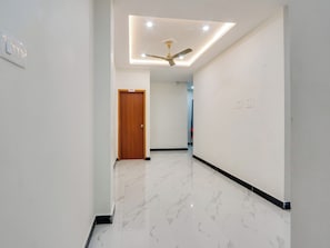 A hallway with a wooden door, a ceiling fan, and a recessed light fixture. - Hotel O Arjun Residency (Khammam)