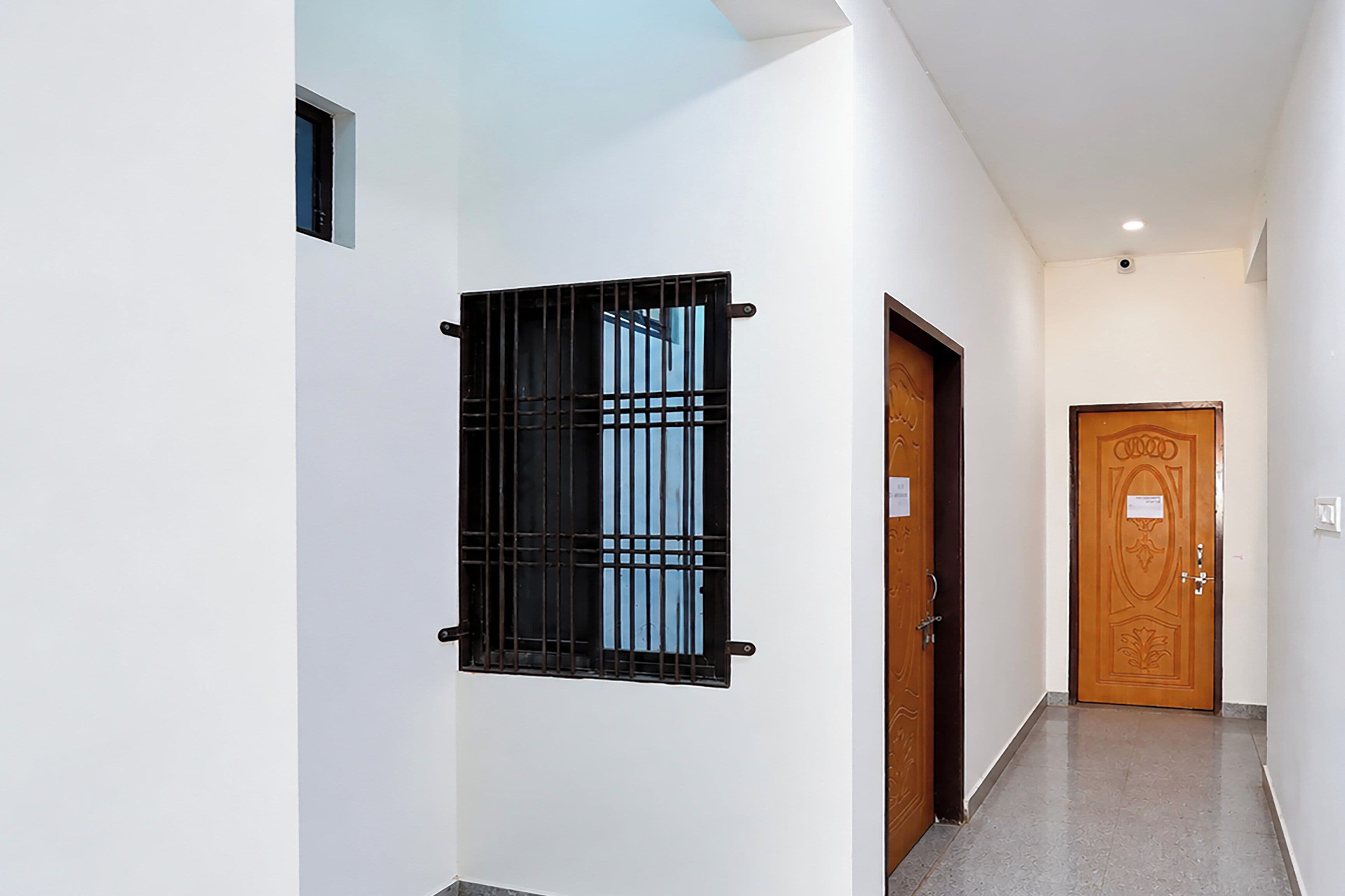 A hallway with a wooden door, a window with metal bars, and a light switch on the wall.