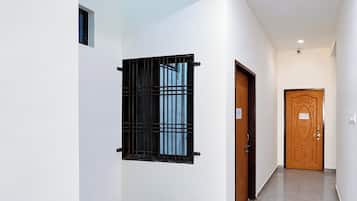 A hallway with a wooden door, a window with metal bars, and a light switch on the wall.