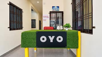A reception area with a green artificial grass table, a sign reading 'OYO', and a small potted plant.