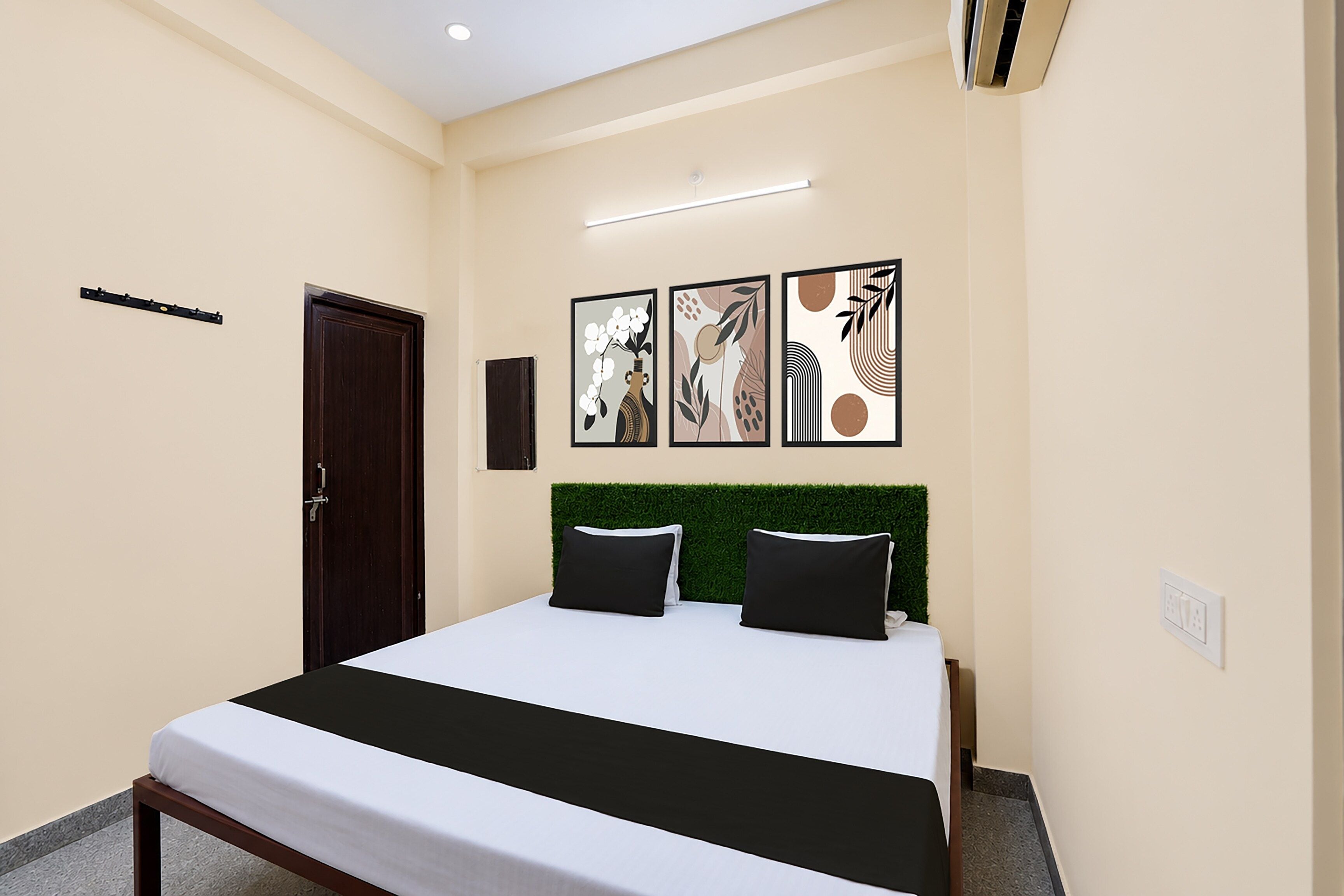 A hotel room with a bed, a door, a wall-mounted air conditioner, and three framed artworks.