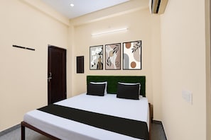 A hotel room with a bed, a door, a wall-mounted air conditioner, and three framed artworks. - Hotel O A.R Palace (Bakshi Ka Talab)