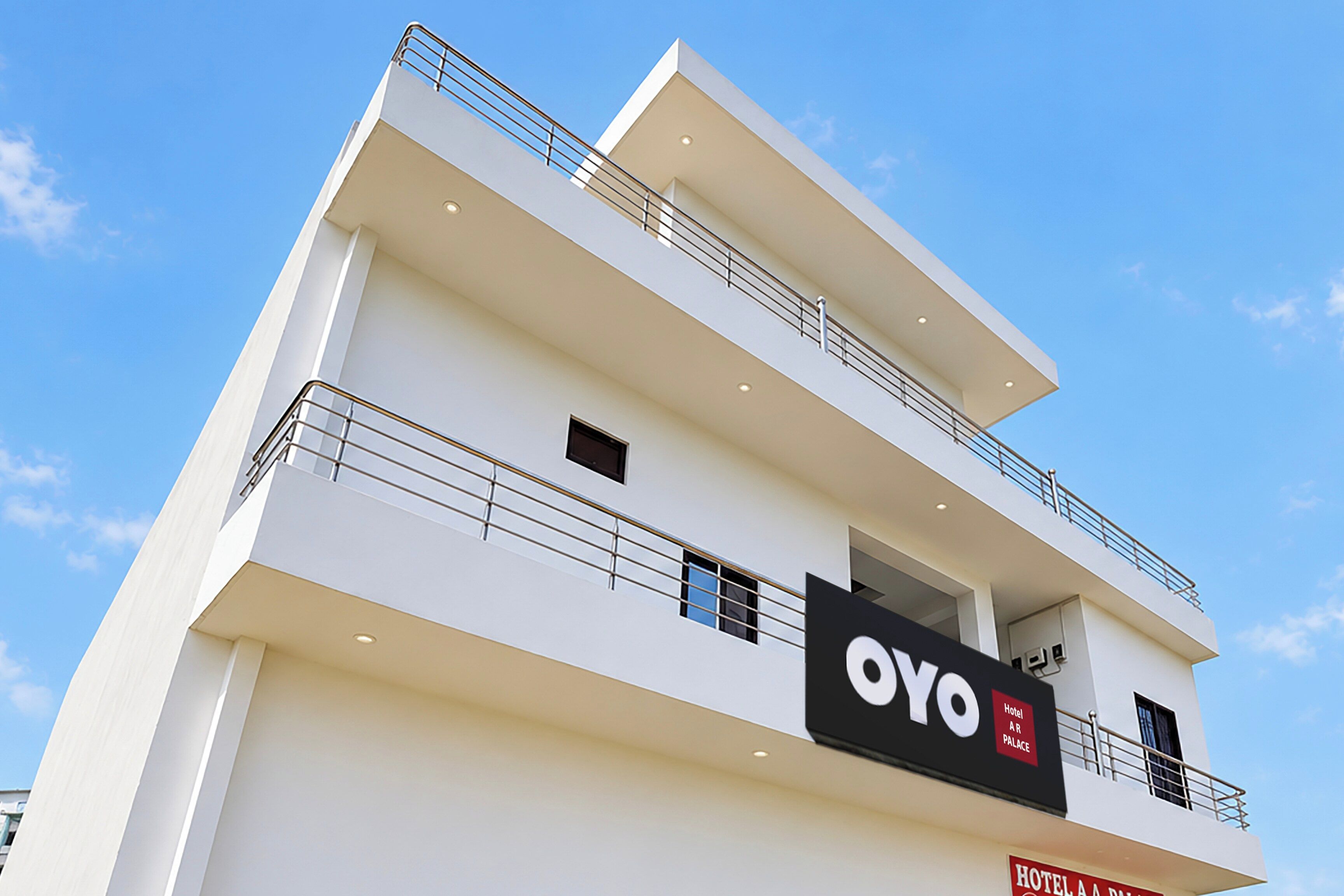 A modern hotel building with a prominent 'OYO' sign, multiple balconies, and a clear sky.