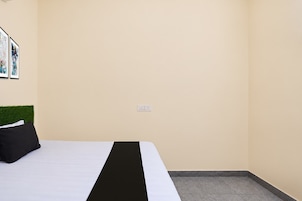 Una habitación de hotel con cama, cabecera de pared verde y toma de corriente.