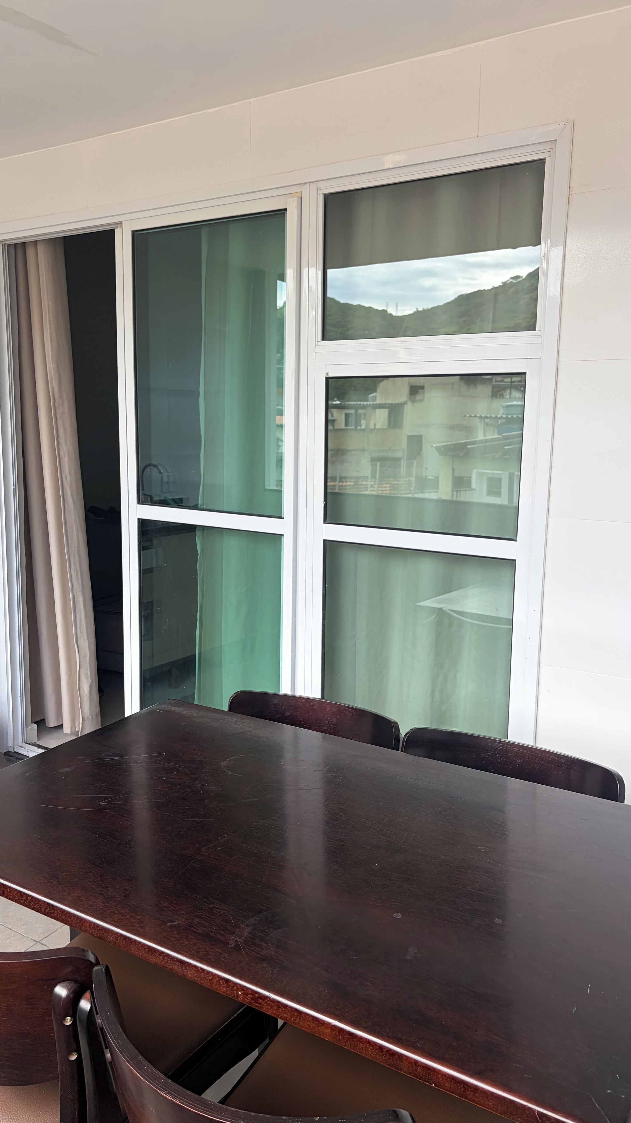 A conference room with a large table and chairs, large windows with curtains, and a view of buildings and hills.