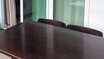 A conference room with a large table and chairs, large windows with curtains, and a view of buildings and hills.