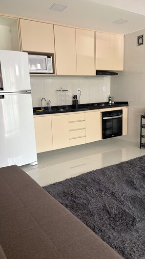 Une cuisine moderne avec des meubles de couleur beige, un réfrigérateur blanc, un four à micro-ondes et un four noir.