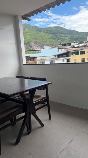 Un balcon avec une table et des chaises, une vue sur un paysage vallonné et des bâtiments en arrière-plan.