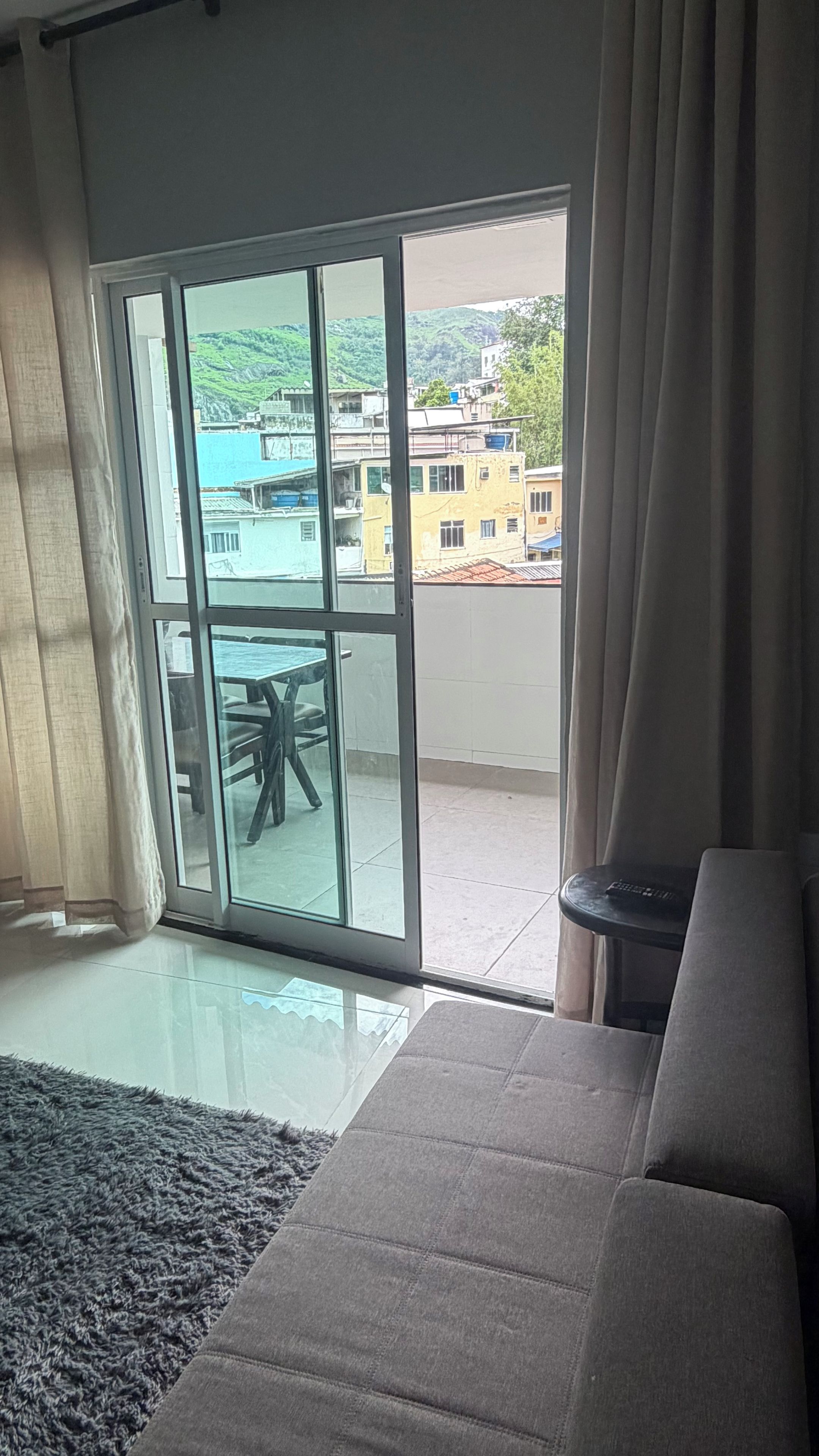 Een kamer met een grote glazen schuindeur die leidt naar een balkon, een grijze bank en een kleine tafel.