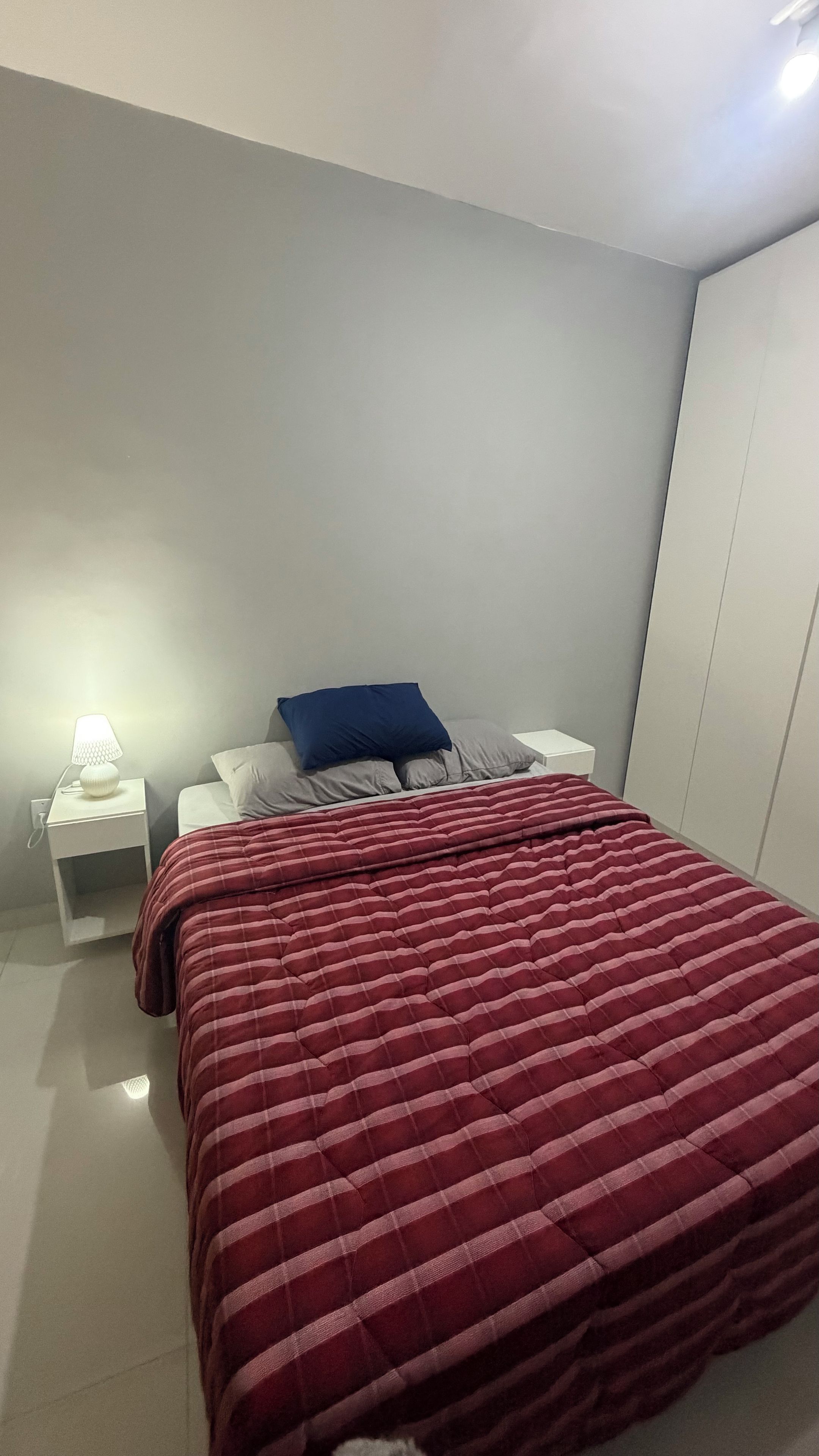 Een slaapkamer met een bed, een nachtkastje, een lamp en een kledingkast.