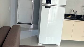 A compact living space with a sofa, a white refrigerator, a microwave, and a small kitchen area.