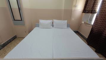Habitació individual amb un llit blanc, dos almoinos, un capçal de llit, un aire condicionat fixat a la paret i una finestra amb cortines estampades.