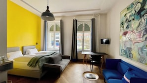 Une pièce avec un lit, un bureau, un canapé bleu et un tableau accroché au mur.