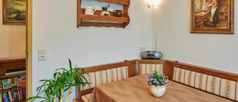 Un coin repas comprenant une table, des chaises, une plante en pot, une étagère avec des ustensiles de cuisine et un tableau accroché au mur.