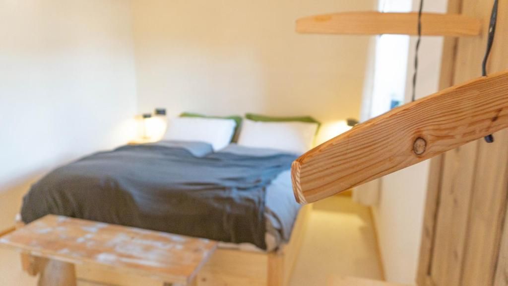 Ein Bett mit dunkler Decke und Kissen, ein hölzernes Kopfende und ein kleiner Tisch mit weißer Oberfläche.