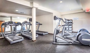 Un gimnasio con cintas de correr, elípticas y una banca de pesas.