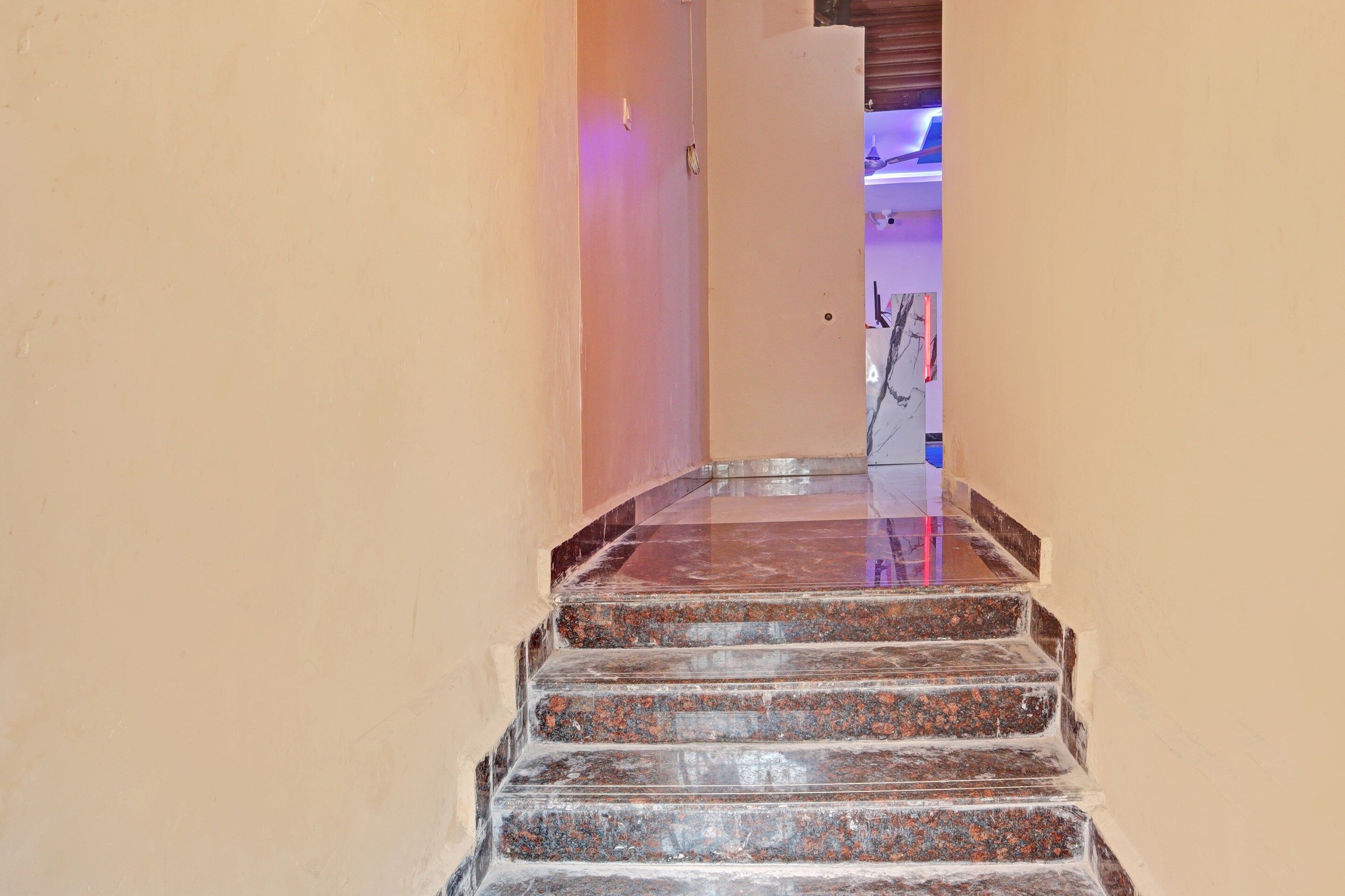 A staircase with a polished stone finish leading to a room with a purple-lit ceiling.