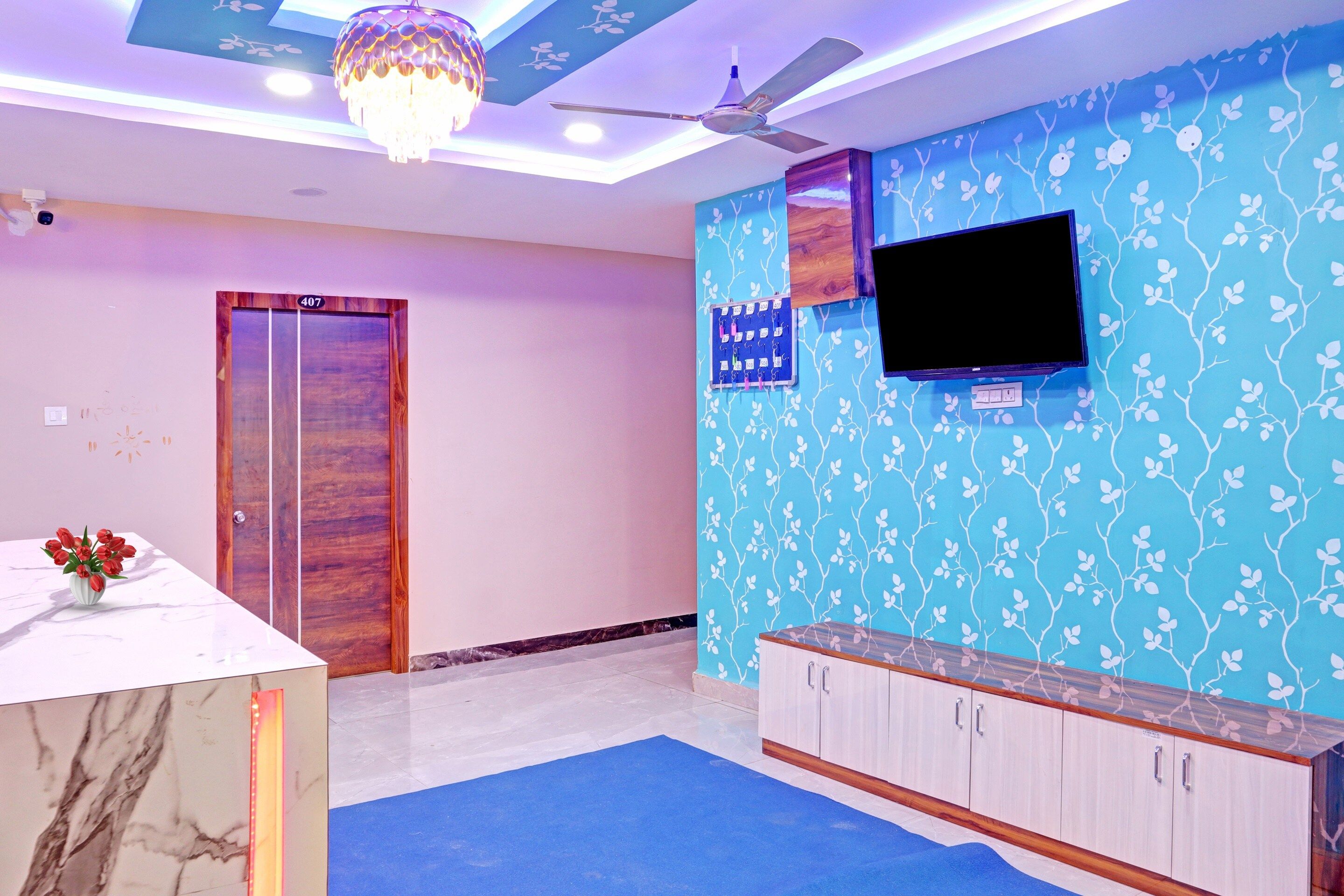 A room with a blue patterned wall, a television mounted above a wooden cabinet, and a ceiling fan.
