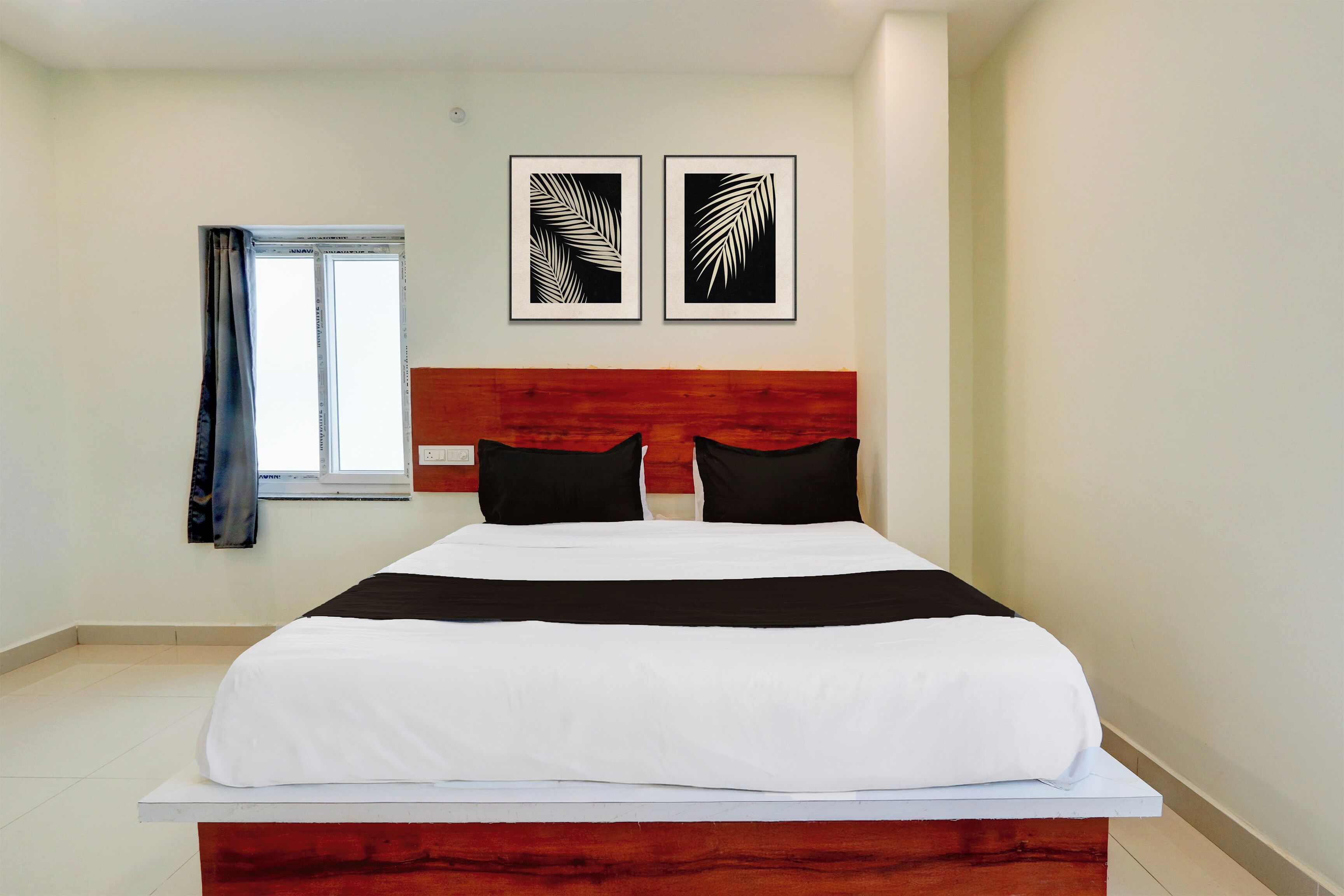 Ein Hotelzimmer mit einem Bett, einem Fenster mit Vorhängen und zwei gerahmten Kunstwerken an der Wand.