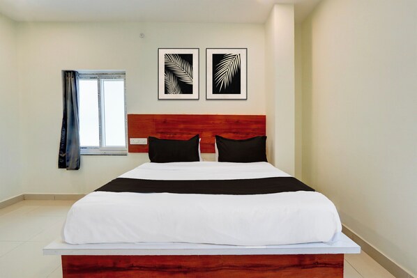 A hotel room with a bed, a window with curtains, and two framed artworks on the wall.