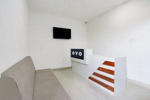 A minimalist room with a grey sofa, a flat-screen TV mounted on the wall, and a reception desk with a sign that reads 'OYO'. - Super Hotel O RB Classic Inn (Karimnagar)