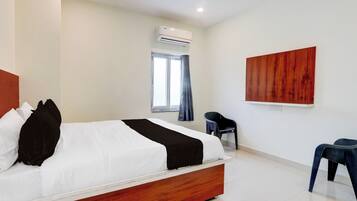 A hotel room with a bed, a desk, a chair, an air conditioning unit, and a window with curtains.